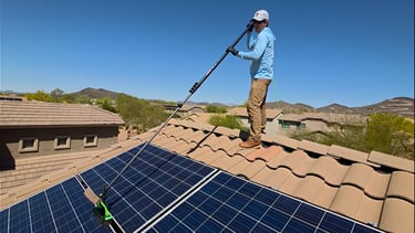 man standing on roof washing solar panel