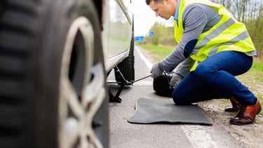 a man in a yellow vest is fixing a tire on a car