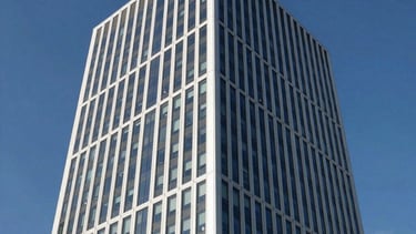 A professional architectural photograph of a sleek, modern corporate office tower in a North American / International Business hub. The image features high-contrast lighting, sharp glass reflections, and a palette of white, gray, and deep blue against a clear sky.