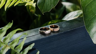 Fotografía premium de detalle de anillos de bodas reodeados de plantas en un fondo de madera azul en Quito
