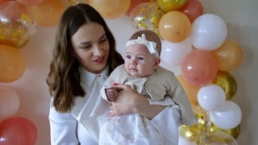 Madre cargando a su bebé en celebración de bautizo con globos color pastel en Querétaro.