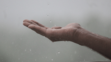 Hand met palm omhoog waarop regendruppels vallen, symbool voor voelen en korte reflectie.