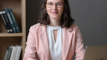 Michelli está em um escritório com caderno e notebook abertos em cima da mesa, há livros no ambiente