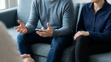 A couple sits on a sofa during a marriage counseling session with a therapist.