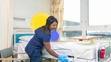 a nurse in scrubs and gloves cleaning a patient's bed