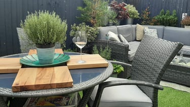 Modern garden patio with grey rattan furnituree, potted herbs, and a glass of wine on a table.