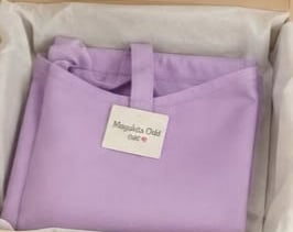 Prenda morada doblada con una etiqueta de marca tipo boutique, dentro de una caja de envío de cartón