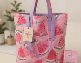 Un bolso de lona rosa con estampado de rodajas de sandía y asas moradas.