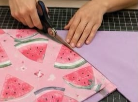 Manos utilizando tijeras de costura para cortar tela de algodón con estampado de sandía.