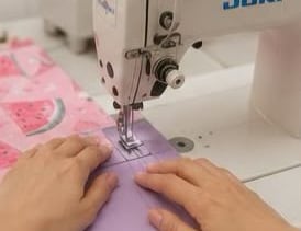 Una persona utiliza una máquina de coser industrial Juki blanca para coser una tela con estampado.