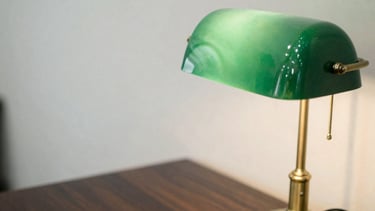 Macro detail of a vintage brass desk lamp on a dark wood desk, soft overcast London daylight, shallow depth of field, forest green accents, editorial film photography.