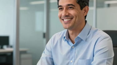 A close-up photograph of a professional South American advisor smiling while working in a modern, light blue and silver office setting with clean glass partitions and steel blue accents, conveying trust and transparency.