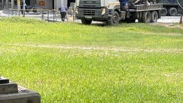 A white industrial vacuum truck parked outside a large concrete factory facility on a sunny day.
