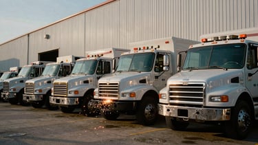 A line of heavy-duty commercial welding trucks parked outside an industrial office building in Forney Texas, bright morning sun reflecting off steel toolboxes, high-contrast utility style, 35mm