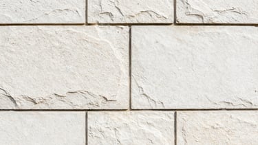 Tight macro detail shot of clean, precisely aligned stone blocks in a retaining wall, showing fine grout lines and texture, bright morning daylight, sharp focus.