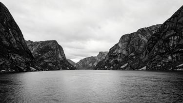 Extremely wide black and white shot of a vast Norwegian fjord landscape, empty, silent, with dramatic high contrast between water, sky, and towering rock formations, minimalist, 35mm