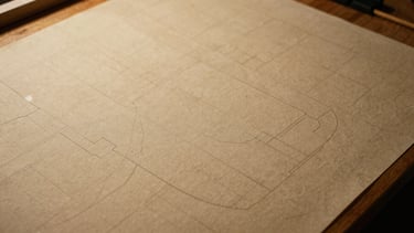 Overhead flat-lay of technical pattern pieces marked with chalk on heavy canvas, warm workstation light
