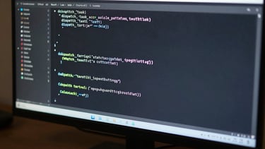 Wide close-up of a monitor displaying a terminal window with multiline monospace code — a function call named dispatch_task with parameters for task type, budget, and callback URL — flat even overhead studio lighting, no glare, dark desk surface below screen partially visible