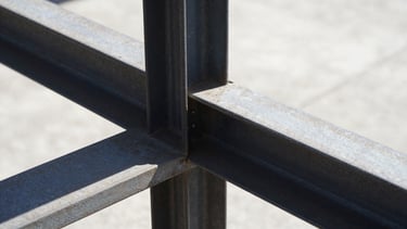 Extreme close-up of structural steel connection with high-contrast shadows, raw metal texture under harsh direct sunlight, stark industrial photography.