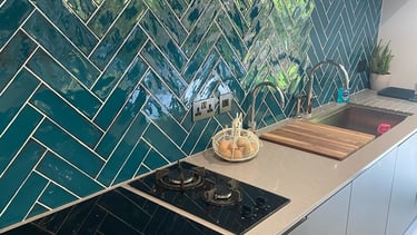 A kitchen backsplash with teal tiles laid in a herringbone style.