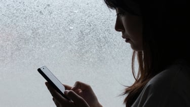 A subtle shot of a woman's silhouette against a frosted glass window, holding a phone down by her side, symbolizing a moment of choosing presence over the screen.
