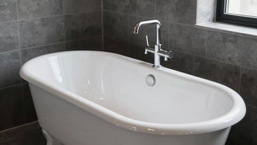 A high-end, clean photography of a gleaming white reglazed bathtub in a minimalist New York City apartment. The bathroom features premium dark grey tiles and bright natural light. The aesthetic is industrial yet luxurious, showing the high-gloss finish of the porcelain. North American / US - New York City.