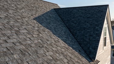 A high-resolution wide-angle shot of a newly installed, dark gray asphalt shingle roof on a beautiful North American residential home in Jackson Township, New Jersey. The craftsmanship is precise, the sky is clear blue, and the lighting is warm afternoon sun highlighting the texture of the shingles.