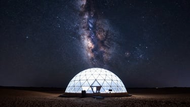 Ultra-wide environmental shot of a single glowing geodesic dome in the vast desert, dwarfed by the towering arc of the Milky Way, long-exposure 35mm night photography.