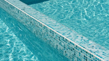 Macro architectural photograph of precise turquoise mosaic pool tiles perfectly aligned along a sharp zero-edge coping, shimmering water, bright daylight, 35mm