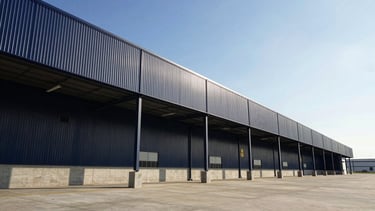 Low-angle architectural perspective of a modern concrete and steel logistics terminal, crisp natural daylight, deep navy shadows, 35mm editorial photography