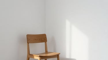 A serene corner of a minimalist studio, clean white walls, a single wooden chair, natural soft daylight casting gentle shadows, editorial atmosphere