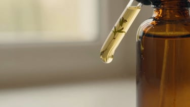 Close-up macro shot of a rich, golden botanical oil texture swirling gently in an amber glass bottle, soft golden-hour window light, shallow depth of field, muted cream and botanical green tones.