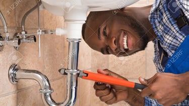 Un plombier professionnel utilisant une clé à molette pour réparer le siphon d'une maison à Yaoundé