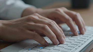 Close-up of hands typing on a modern keyboard with soft blue light reflection, representing data entry and analysis in a professional setting.