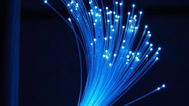 Abstract photography of fiber optic cables glowing in bright blue within a dark navy infrastructure environment. High-speed data transmission concept.