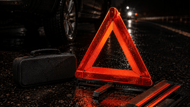A red reflective emergency warning triangle and roadside kit placed on a wet road at night.
