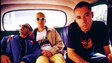 Os três integrantes dos Beastie Boys sentados no banco traseiro de um carro.