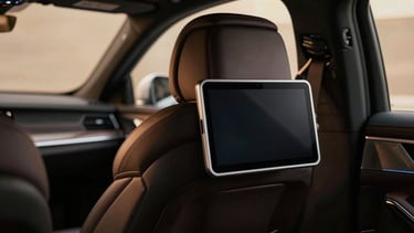 Close-up of a premium leather back seat of an executive sedan, modern tablet mounted on the headrest, warm ambient cabin light, shallow depth of field, cinematic.