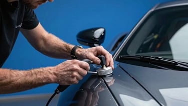 Professional high-end photography of a male detailer's hands applying a ceramic coating to a glossy charcoal metallic supercar under cinematic electric blue studio lighting, International / Global style.