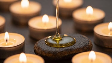 Macro shot of warm oil trickling onto basalt stones, soft glowing golden candlelight, shallow depth of field, 35mm