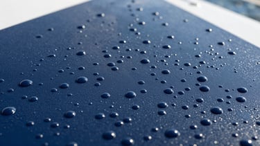 Extreme close-up of perfectly spherical water beads on a deep navy boat gelcoat, bright morning light, sharp focus.