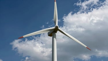 Low-angle heroic shot of wind turbine blades cutting through low clouds, dramatic natural sunlight, 35mm crisp industrial photography