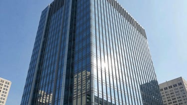 A modern corporate building with a sleek glass facade reflecting a bright blue sky, located in a bustling North American financial district. The architectural style is futuristic and premium, communicating enterprise-readiness, innovation, and technological advancement.