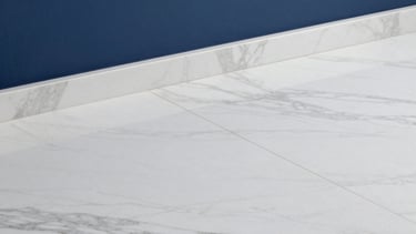 Detailed photography of a premium white marble floor meeting a deep blue wall, representing the high-end material sourcing capabilities of the firm.
