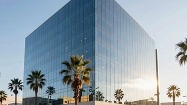 A professional architectural photograph of a sleek, modern glass office building in Irvine, Southern California, under a clear bright sky. The scene features palm trees and clean, minimalist landscaping. The lighting is bright and airy, reflecting efficiency. Colors include deep steel blue glass, pale blue sky, and warm gold sunlight glinting off the facade.