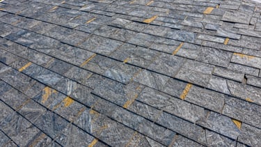 Close-up of flawless architectural shingle alignment on a steep roof, bright midday sun, deep slate tones.
