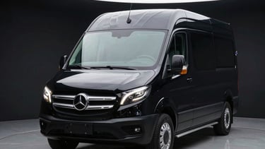 A sleek black commercial vehicle parked under dramatic studio spotlighting, crisp reflections on the hood, high-contrast setup.
