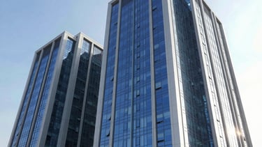 Professional wide-angle photography of a modern energy corporation building exterior in Maslak, Istanbul, Turkey. The structure features reflective blue glass and white steel accents under a clear bright sky. The mood is reliable and forward-thinking, emphasizing sustainable energy architecture.