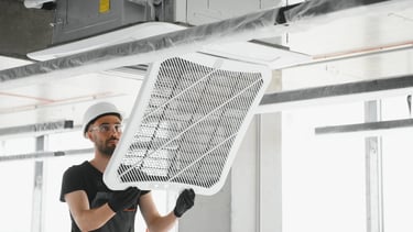 Technician in a hard hat installing a ceiling cassette air conditioning unit and filter.