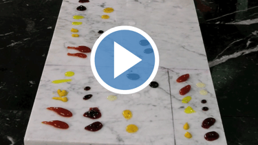 Drops of colorful culinary sauces and glazes arranged on a white marble slab for stain testing.